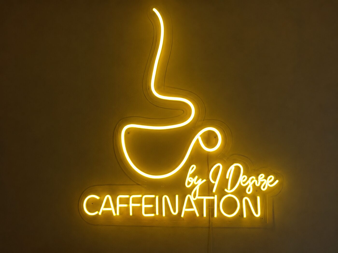 Glowing neon Caffeination by I Desire sign inside the café